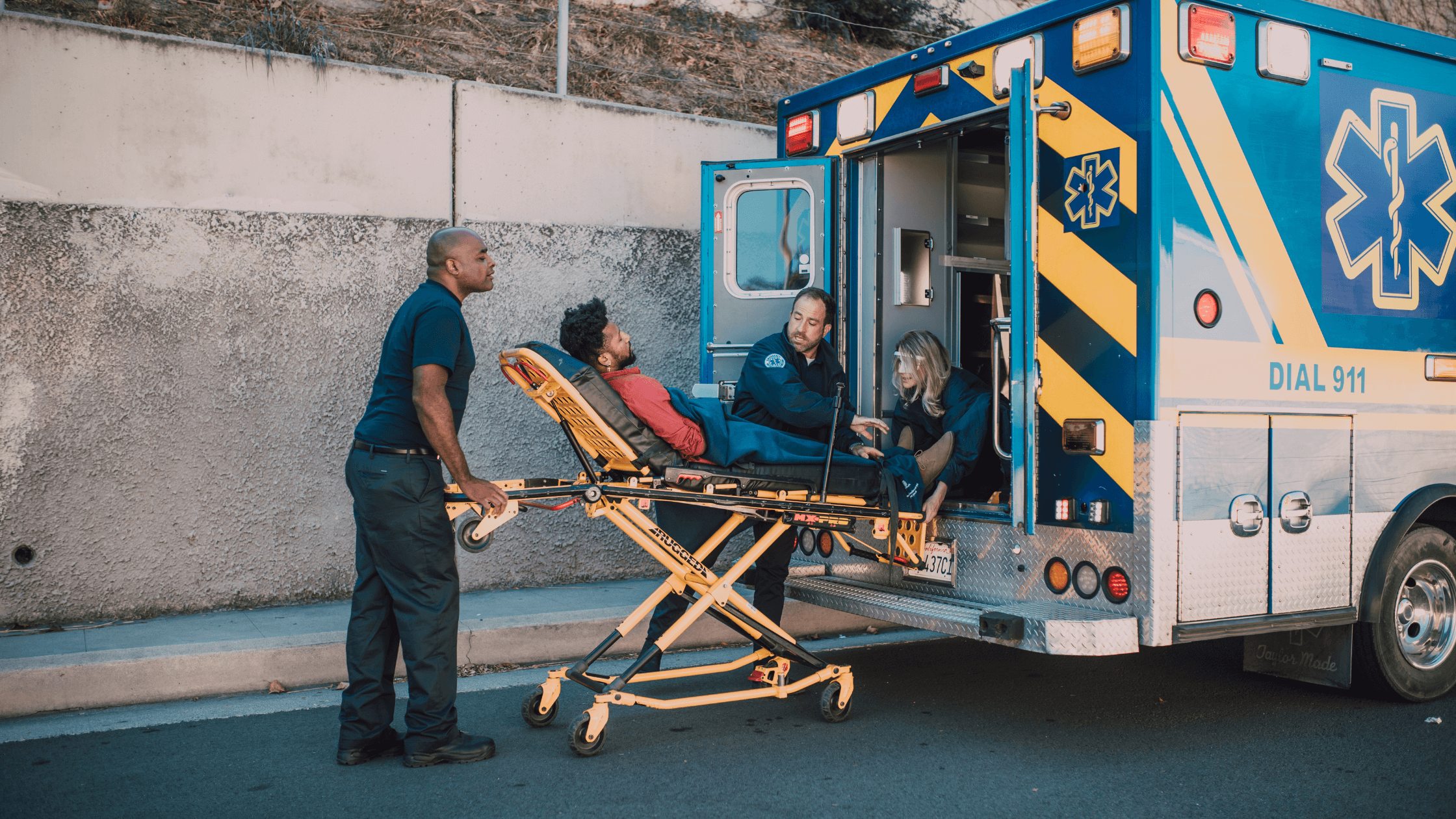 Emergency Medical Technicians (EMTs) attending to a patient on a stretcher by an ambulance, depicting a life-saving career and high-need jobs in healthcare trades.