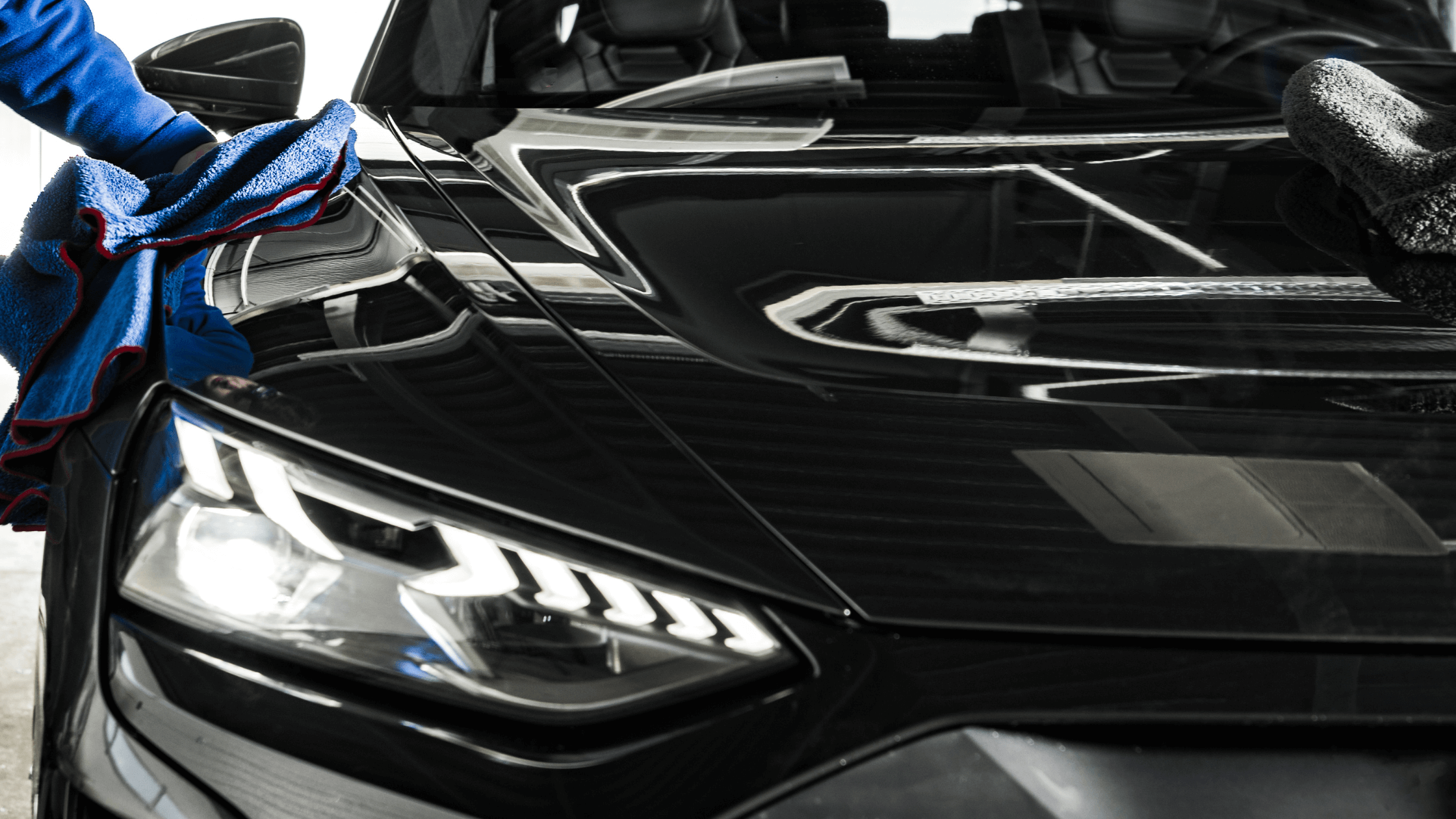 A professional auto detailer polishing the gleaming black hood of a luxury car, illustrating the meticulous work involved in a thriving auto detailing career and skilled trade.