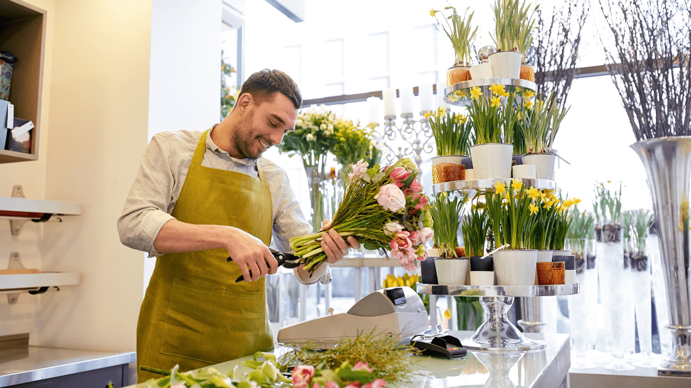 A smiling male florist, expertly trimming flowers in a vibrant flower shop, symbolizing a successful career change to a fulfilling floral design trade.