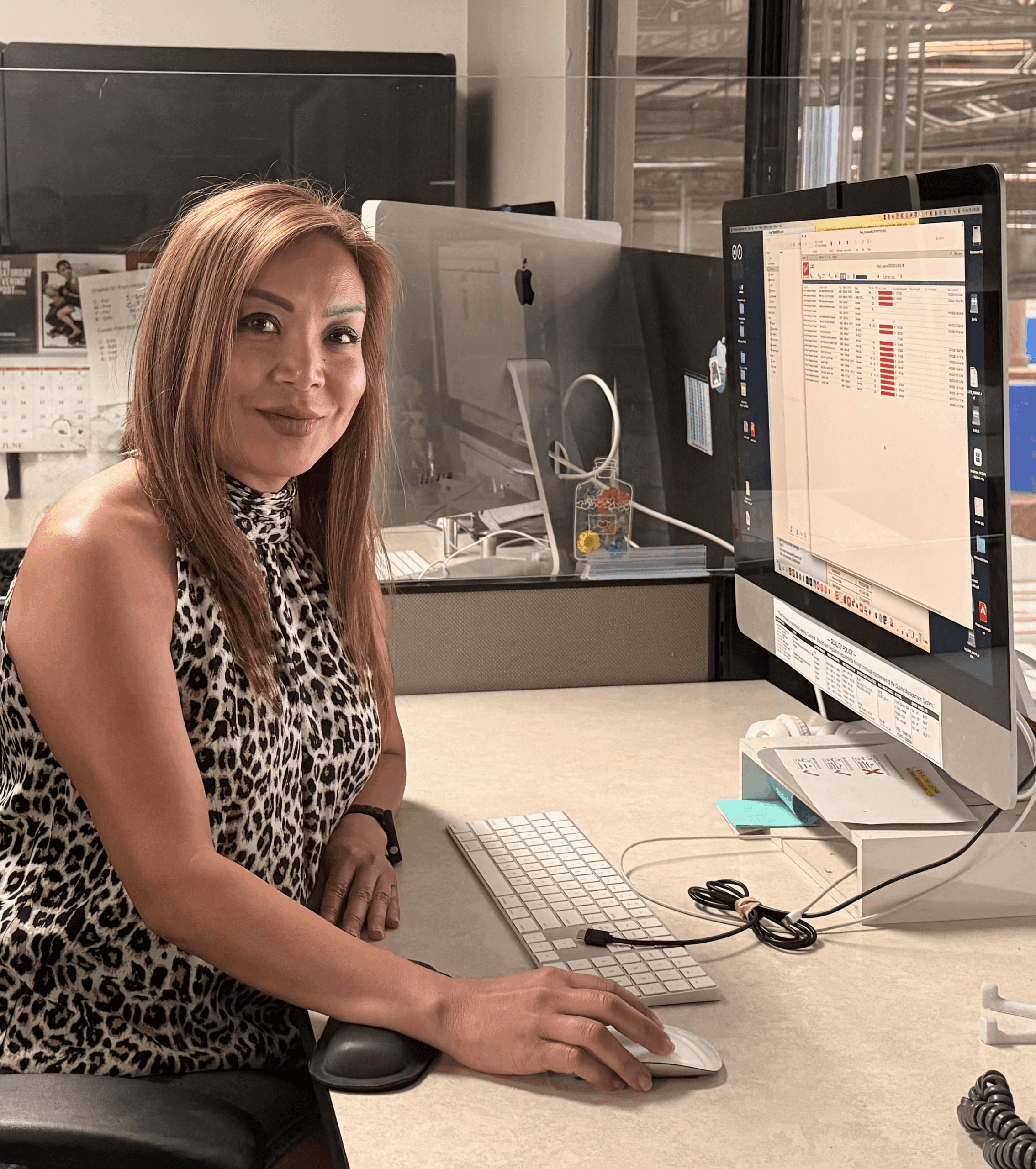 A professional smiling at her desk in an office, representing a hands-on career in the printing and prepress industry.