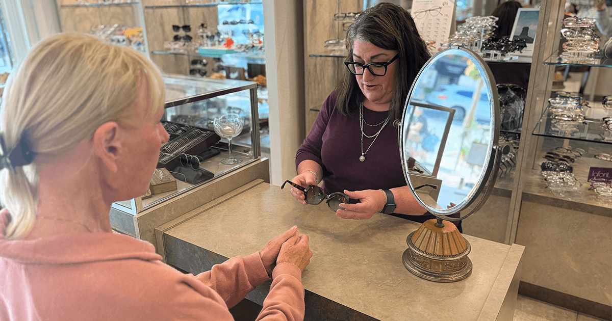 Suzanne helping a customer try on glasses in a retail store, symbolizing a successful service trade career and entrepreneurship.