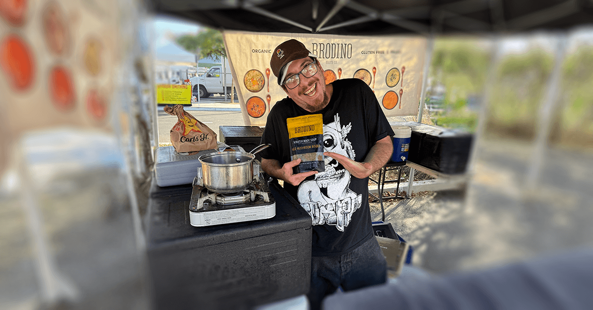 Julius presenting a food product at a market stall with a portable stove, representing a successful culinary entrepreneurship and service trade career.