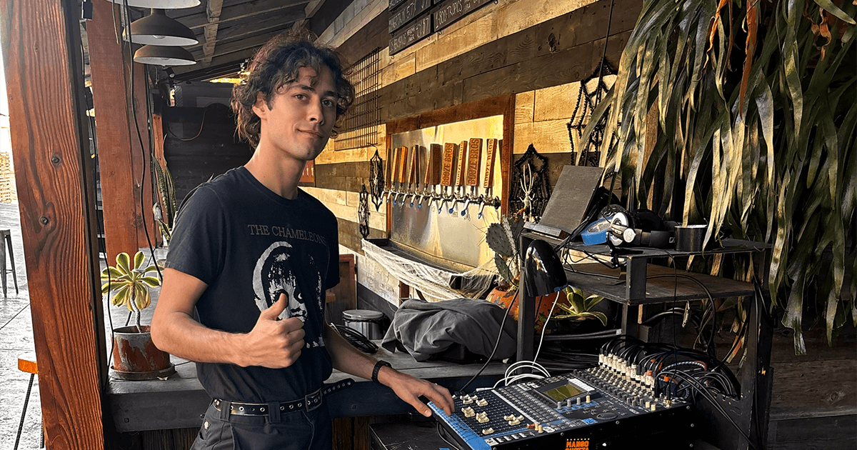 Niko giving a thumbs-up while standing next to an audio mixing board, symbolizing a successful and rewarding creative trade career in music technology.