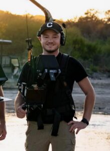 Logan Powaski, a cinematographer, smiling in a camera stabilizer harness during an outdoor shoot at sunset