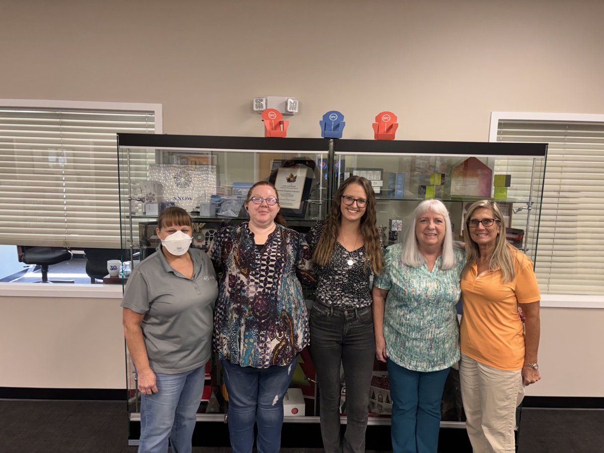 Hannah, a customer service manager, standing with her four-person customer service team in front of a display case in their company office