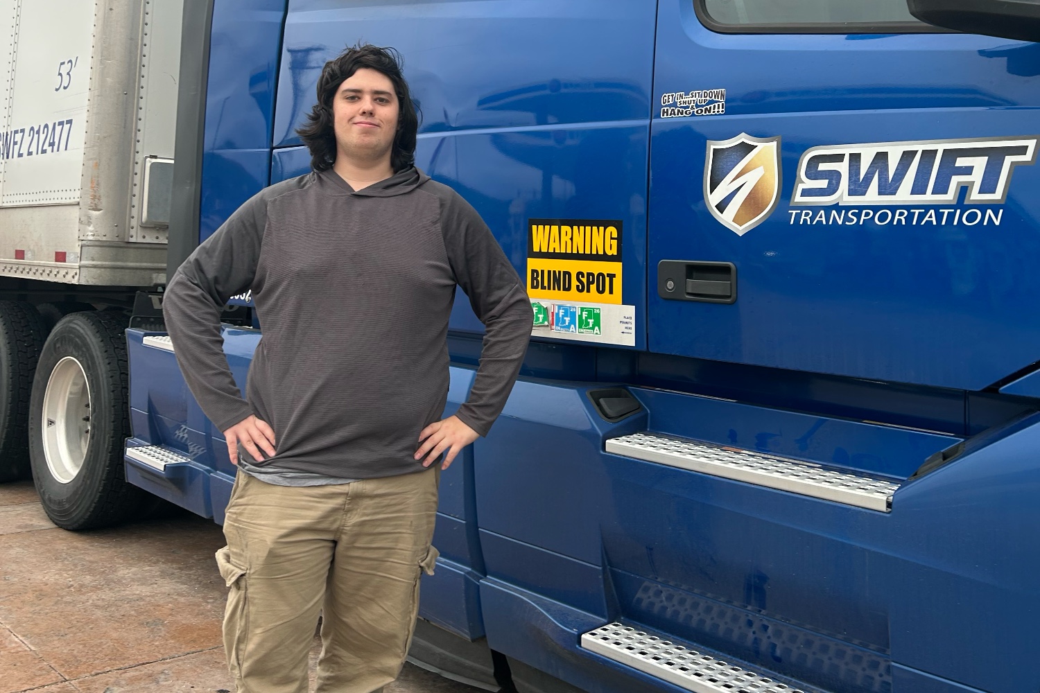 Caden, a commercial truck driver, standing in front of his blue Swift Transportation semi truck