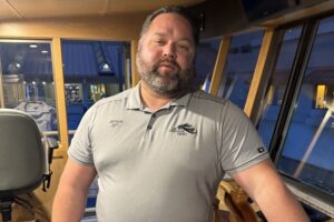 Captain Jeff at the wooden ship's wheel in the wheelhouse of the Lake Coeur d'Alene Cruises dinner boat